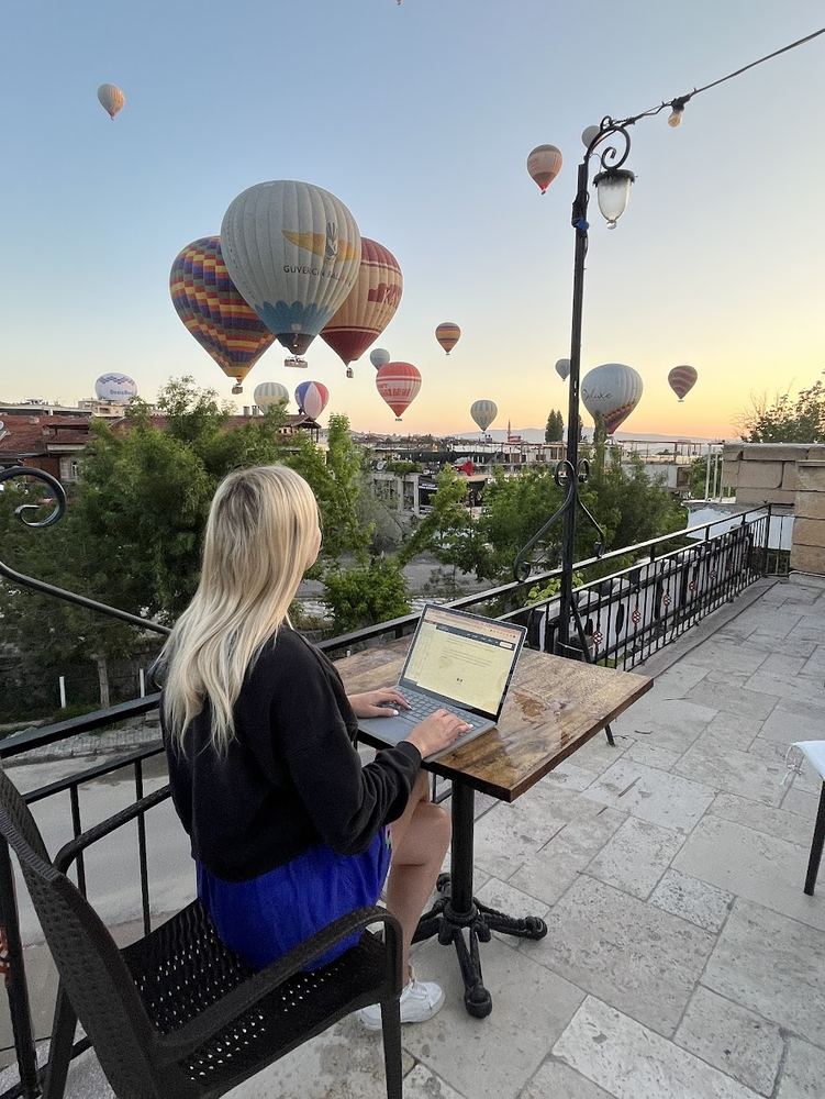 Andrae working on a rooftop in Cappadocia with hot air balloons in the sky
